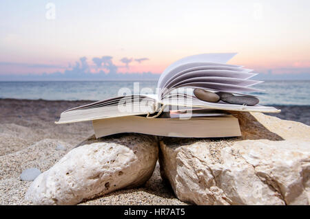 Open book at beach on a pile of books near the sea during summer sunset Stock Photo