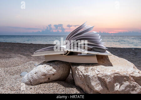 Open book at beach on a pile of books near the sea during summer sunset Stock Photo