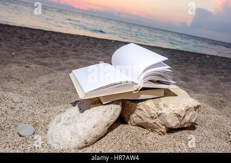 Open book at beach on a pile of books near the sea during summer sunset Stock Photo