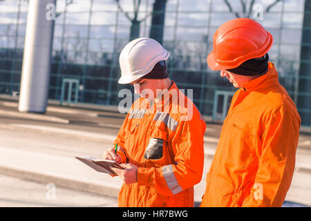 team of  young engineers discussing project and writing in the note book.. The wear overalls and safety helmets. Business modern background Stock Photo