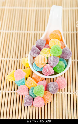 Colorful candies, jelly sugar in white spoon on bamboo mat. Stock Photo