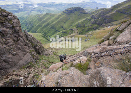 A hiker navigates steep chain ladders to get up a cliff in Royal Natal National Park, South Africa on the Amphitheater Hike. Stock Photo