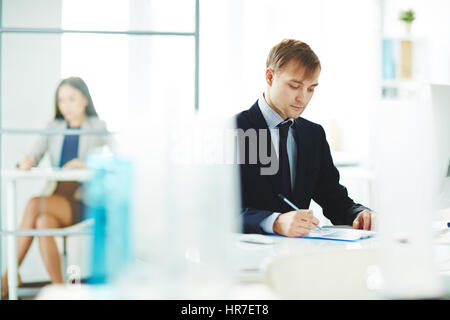 Portrait of young business analyst checking statistics report with graphs while sitting at workplace in modern light office Stock Photo