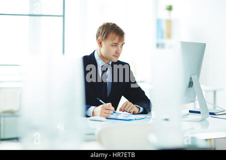 Portrait of successful young business analyst busy working alone in modern office, checking statistics report with graphs while sitting at computer de Stock Photo