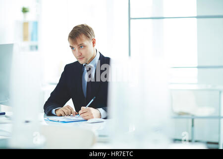 Portrait of successful young business analyst busy working alone in modern office, checking statistics report with graphs and looking at computer scre Stock Photo