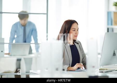 Portrait of confident young businesswoman busy working at desk in modern office, looking at computer screen and typing Stock Photo