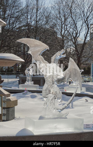 Ice sculpture in Ottawa, on a sunny day with ice covered trees behind.  Ice scupltrure is of a dragon with its wings outstretched. Stock Photo