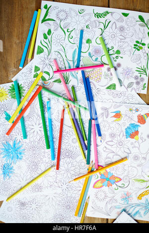 Still life of pages of flowers and mandalas from coloring books and pencils laid on wooden table, high angle view Stock Photo