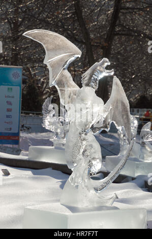 Ice sculpture in Ottawa, on a sunny day with ice covered trees behind. Ice scupltrure is of a dragon with its wings outstretched. Stock Photo