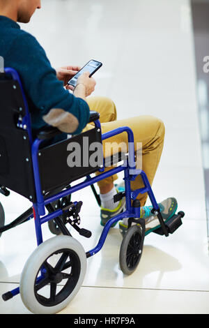 Side view of disabled young man sitting in wheelchair and texting on his smartphone Stock Photo