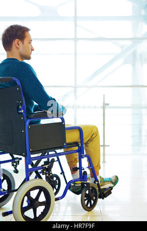 Side view of young man sitting in wheelchair and looking into the distance thoughtfully Stock Photo