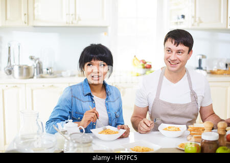 Attractive mixed race woman and her Caucasian husband in apron having lunch together in lovely kitchen Stock Photo