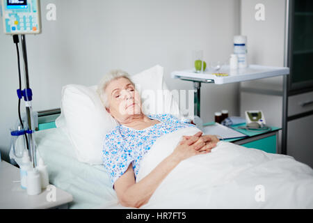 Senior woman asleep on bed after getting her treatment in geriayric hospital Stock Photo
