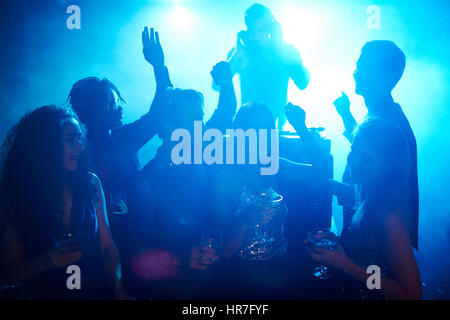 Group of dressed-up young people enjoying DJ concert in fashionable night club, dancing with cocktails and having fun Stock Photo