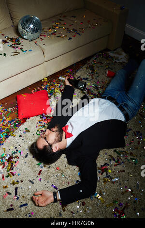 Intoxicated bearded man with bow tie having nap on carpet covered with confetti after wild house party Stock Photo