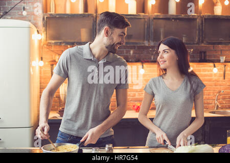 Young beautiful couple in kitchen. Family of two preparing food. Man and woman looking at each other while making delicious pasta. Nice loft interior  Stock Photo