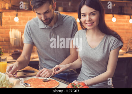 Pizza time. Young beautiful couple in kitchen. Family of two preparing food. Couple making delicious pizza. Woman smiling and looking at camera. Nice  Stock Photo