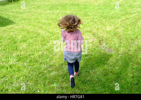 A cute little girl in stripes running in a garden, view from the back Stock Photo