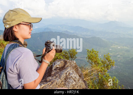 Hiker asian teen girl wear cap and eyeglass with happy holding dslr camera for photography beautiful natural in winter on peak mountain at Phu Chi Fa  Stock Photo