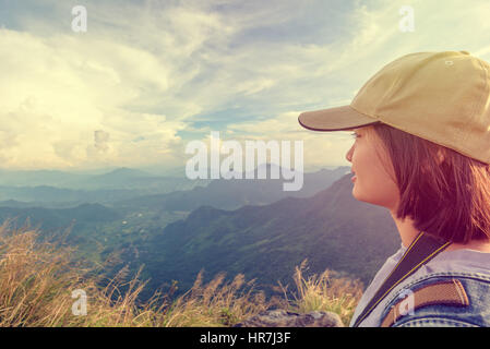 Vintage style hiker asian teen girl wear cap with happy looking beautiful landscape nature on top of high mountain at viewpoint Phu Chi Fa Forest Park Stock Photo