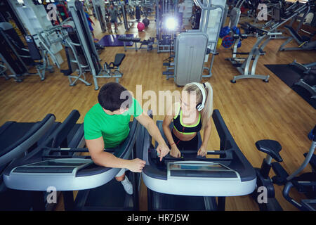 Personal trainer man with athletic girl on a treadmill in the gym. Top view. Stock Photo