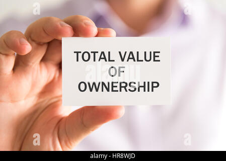 Closeup on businessman holding a card with TOTAL VALUE OF OWNERSHIP message, business concept image with soft focus background and vintage tone Stock Photo