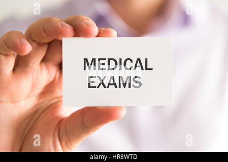 Closeup on businessman holding a card with MEDICAL EXAMS message, business concept image with soft focus background and vintage tone Stock Photo