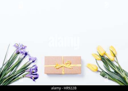 Purple irises, yellow tulips and gift box with bow on white background, top view Stock Photo