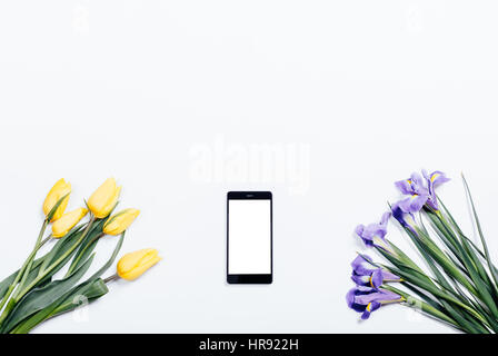 Yellow tulips, purple irises and mobile phone on a white background, top view Stock Photo