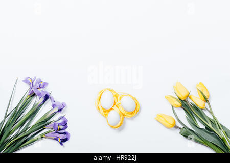 Purple irises, yellow tulips and nest with Easter eggs on white background, top view Stock Photo