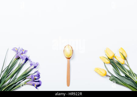 Yellow tulips, purple irises and easter egg with a spoon on a white background, top view Stock Photo