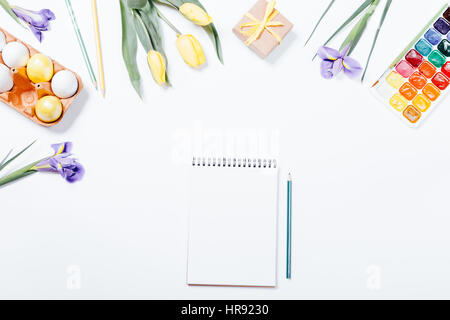 Festive Easter arrangement of flowers, painted eggs, watercolors, notebook and pencil, top view Stock Photo