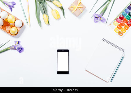 Easter composition: flowers, mobile phone, painted eggs, watercolors and a notebook. Top view. Stock Photo