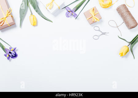 Festive composition on white table: purple and yellow flowers, boxes with gifts, ribbons. Top view, copy space Stock Photo