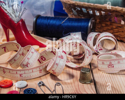 Needle bed with needles and pins, thread on a spool, thread on large spools, scissors, thimble, tape measure, spools of thread in a basket from straw  Stock Photo