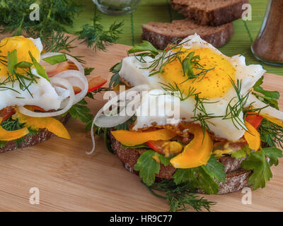 Sandwich with fried eggs on bread with vegetables, peppers, tomatoes, mustard greens, parsley, dill and onion on a wooden board prepared for dinner Stock Photo