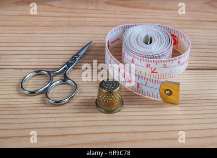 Needle bed with needles and pins, thread on a spool, thread on large spools, scissors, thimble, tape measure, spools of thread in a basket from straw Stock Photo