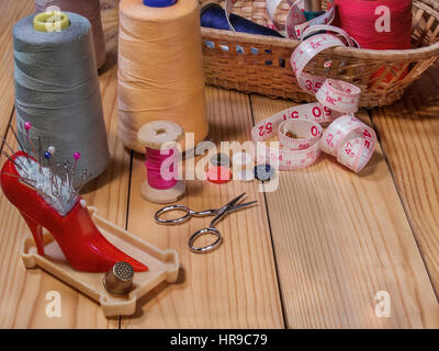 Needle bed with needles and pins, thread on a spool, thread on large spools, scissors, thimble, tape measure, spools of thread in a basket from straw Stock Photo