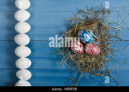 Group of white eggs and three colorful eggs on the blue wooden surface. Easter concept. Stock Photo