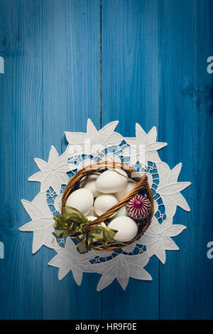 Group of eggs in wicker basket on the blue wooden surface. Easter concept. Stock Photo