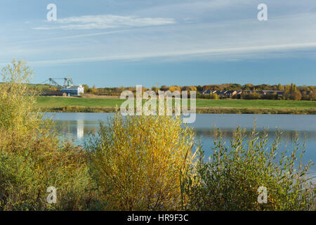 View of dragline, pool and trees showing Autumn colour, on site of former opencast coal mine, St. Aidans RSPB Reserve, West Yorkshire, England, Novemb Stock Photo