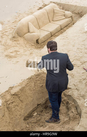 A man digging digging sand as her creates sculptures on a beach on the South Bank in London. Stock Photo