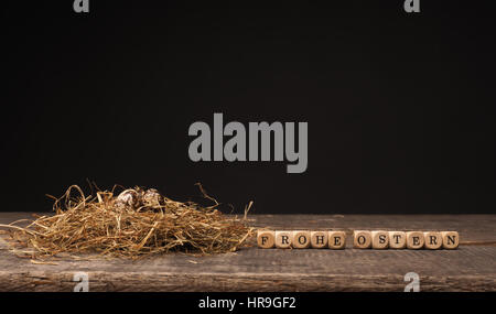 Easter concept with small eggs in a natural nest on wood, German words Happy Easter on wooden dices Stock Photo