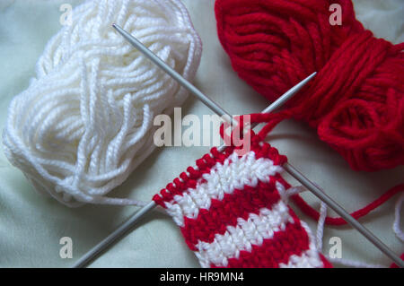 Knitting needles crossed with red and white balls on neutral background. Stock Photo