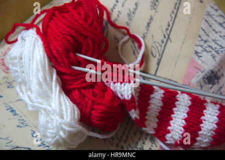 Parallel knitting needles with two balls. Skeins of wool and knitting needles for made a red and white textile scarf with golden background Stock Photo