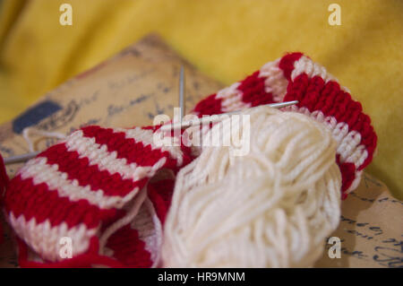 Skeins of wool and knitting needles. Skeins of wool and knitting needles for made a red and white textile scarf with golden background Stock Photo