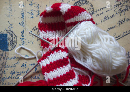 Cross knitting needles. Skeins of wool and knitting needles for made a red and white textile scarf with golden background Stock Photo