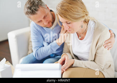 Upset blond-haired woman with tears on her cheeks sitting next to her psychologist while he trying to comfort her Stock Photo