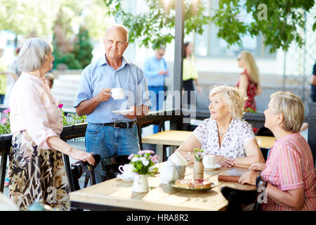 Group of senior friends enjoying each others company in summer cafe and drinking tea with berry pie Stock Photo