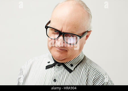 Headshot of male senior with receding hairline and eyeglasses wearing striped shirt looking down thoughtfully and smiling slightly Stock Photo